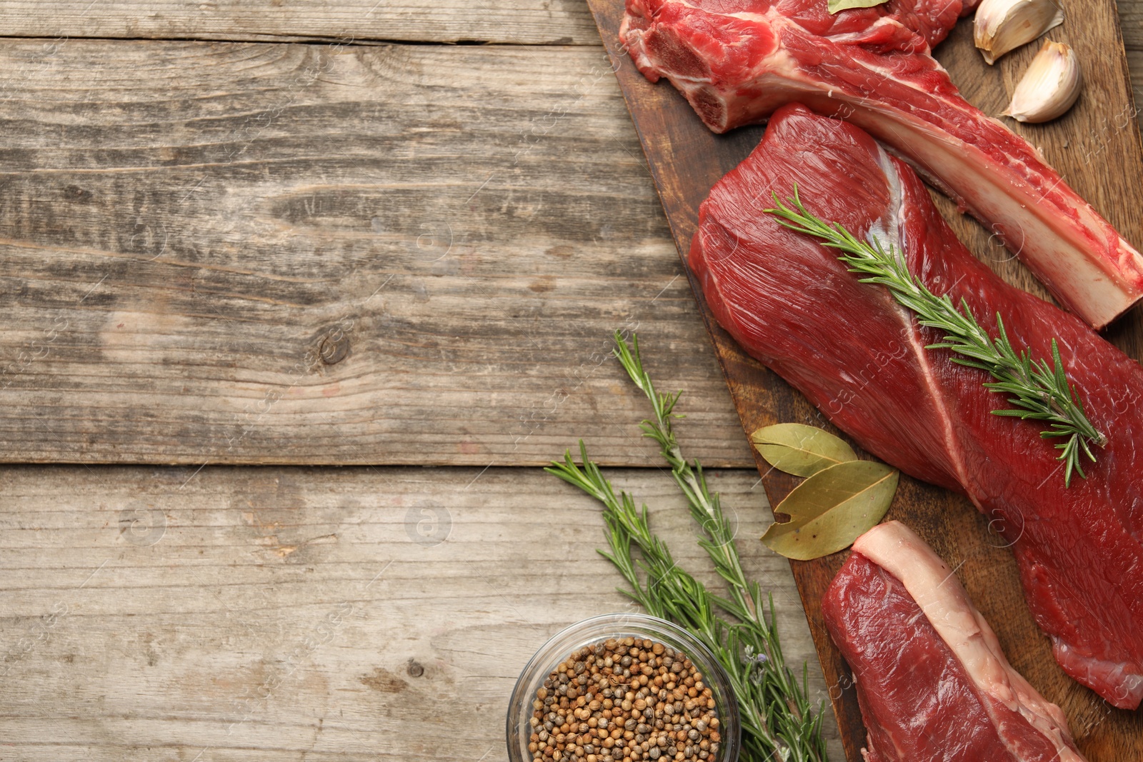 Photo of Pieces of raw beef meat and spices on wooden table, flat lay. Space for text