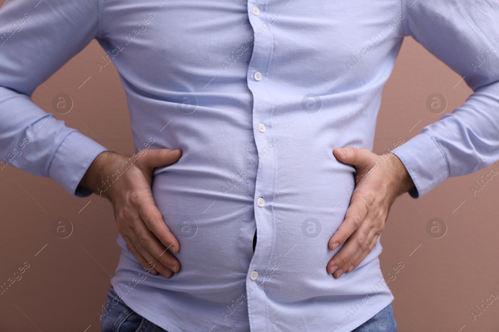 Photo of Man wearing tight shirt on pale pink background, closeup. Overweight problem