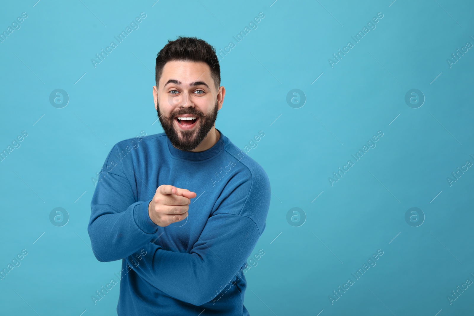 Photo of Happy young man with mustache pointing at something on light blue background. Space for text