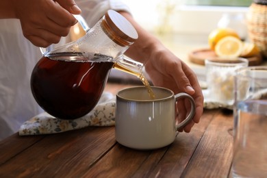 Woman pouring delicious tea into cup at wooden table, closeup