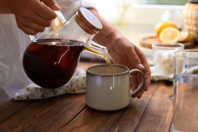 Photo of Woman pouring delicious tea into cup at wooden table, closeup