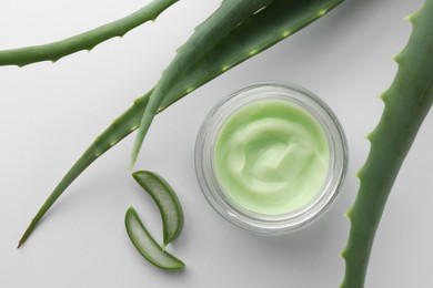 Jar of natural cream and aloe leaves on white background, flat lay