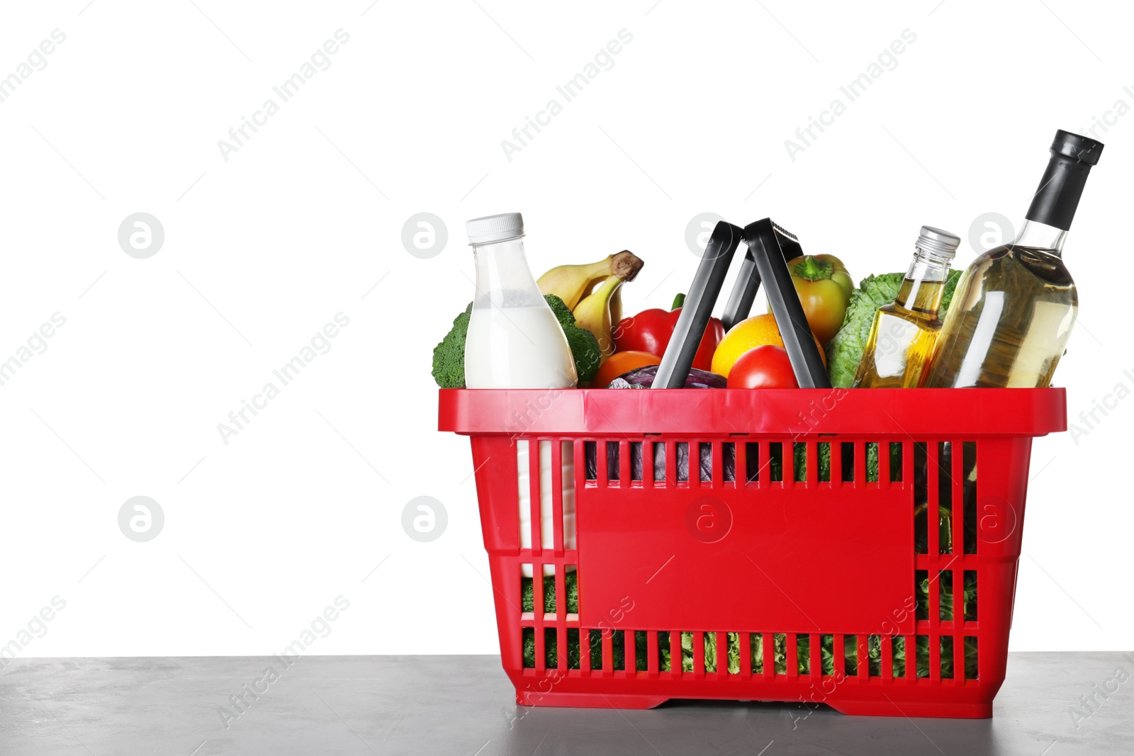 Photo of Shopping basket with grocery products on grey table against white background. Space for text