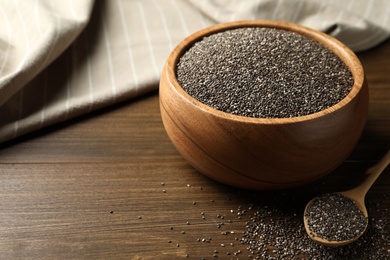 Photo of Bowl and spoon with chia seeds on wooden table. Space for text