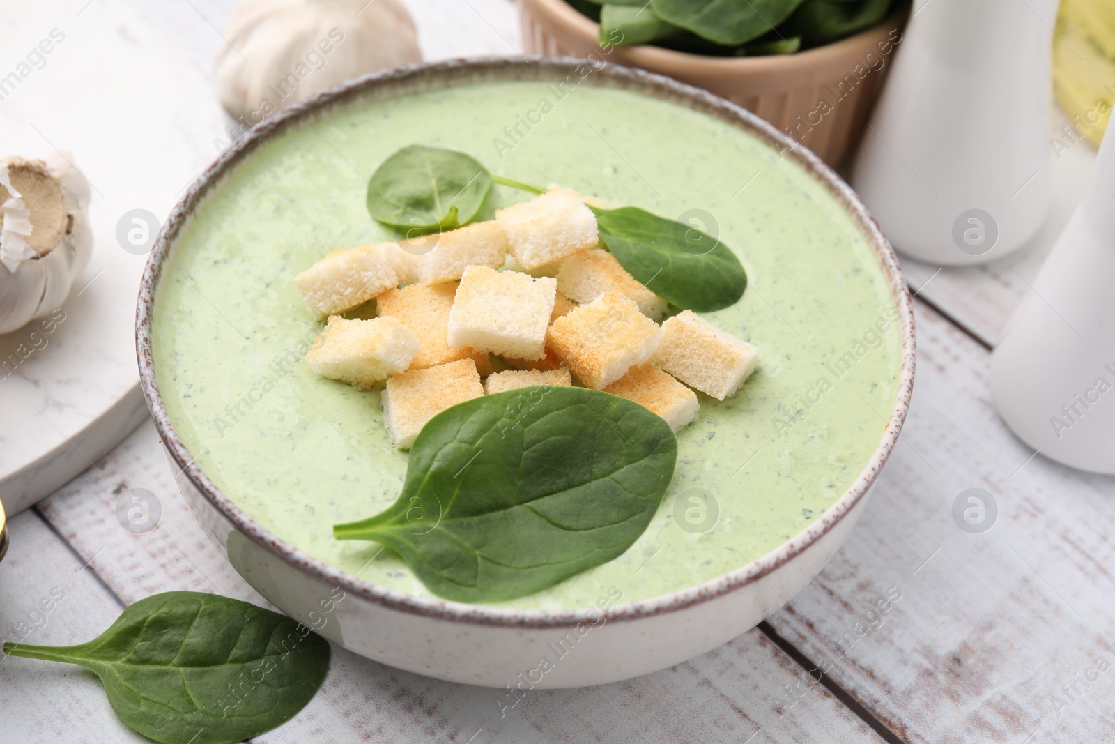 Photo of Delicious spinach cream soup with leaves and croutons in bowl on white wooden table