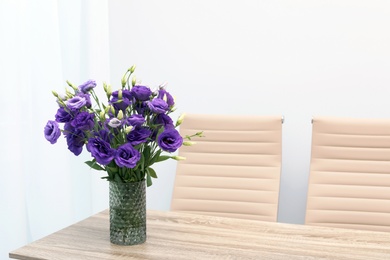 Photo of Beautiful bouquet in vase on wooden table against color background. Stylish interior