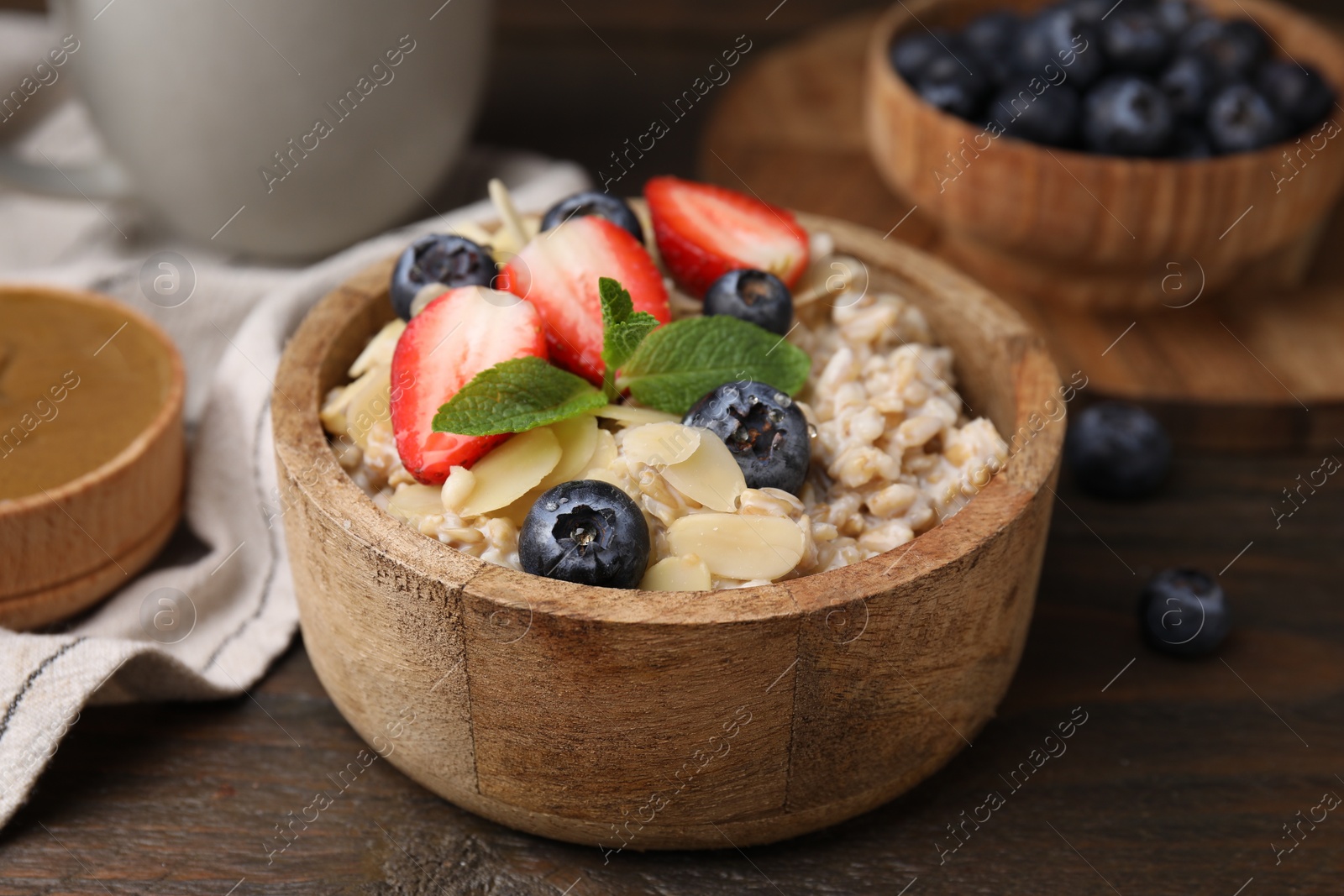 Photo of Tasty oatmeal with strawberries, blueberries and almond flakes in bowl on wooden table, closeup