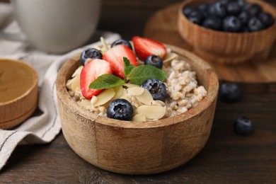 Photo of Tasty oatmeal with strawberries, blueberries and almond flakes in bowl on wooden table, closeup