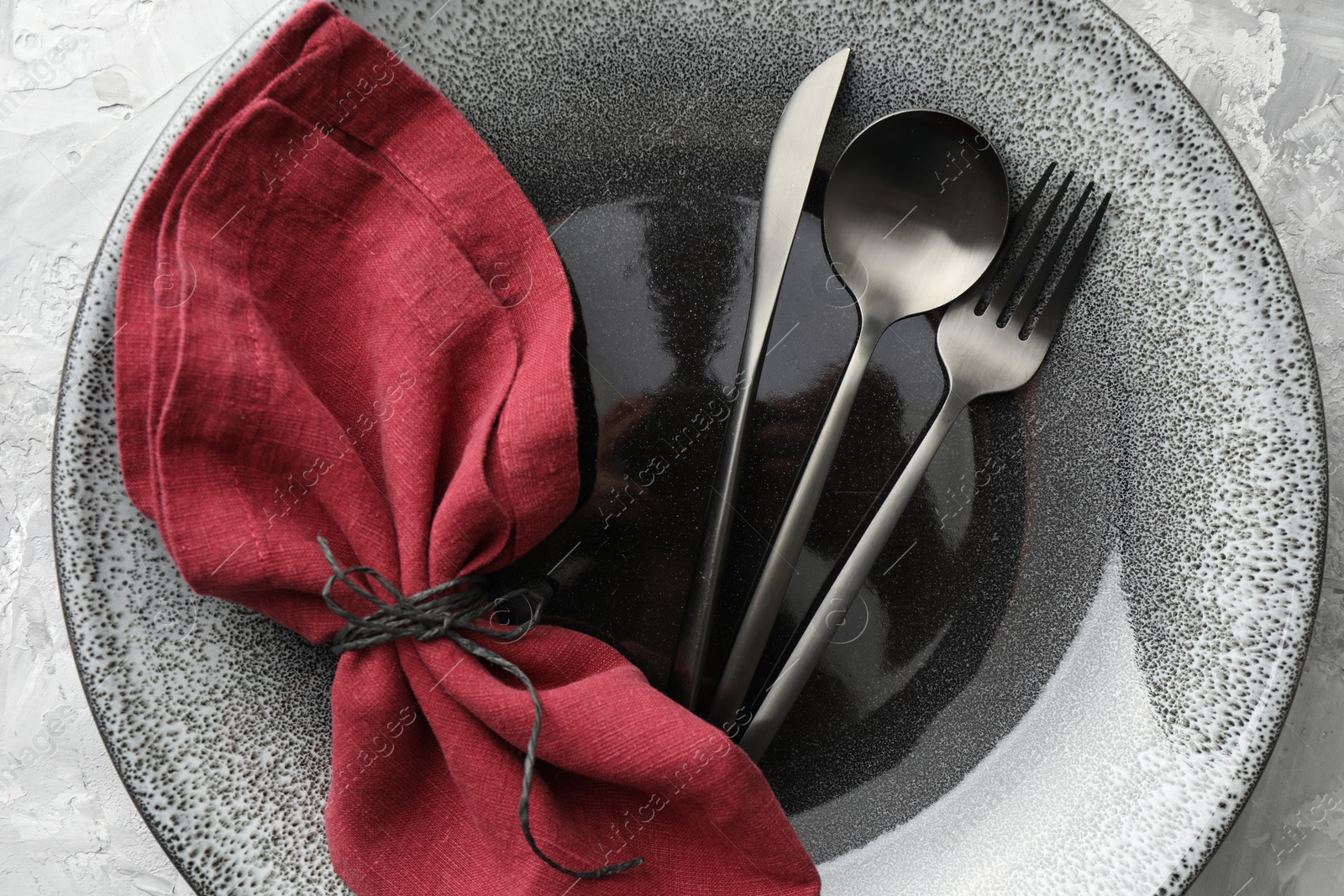 Photo of Stylish setting with cutlery, napkin and plate on grey textured table, top view