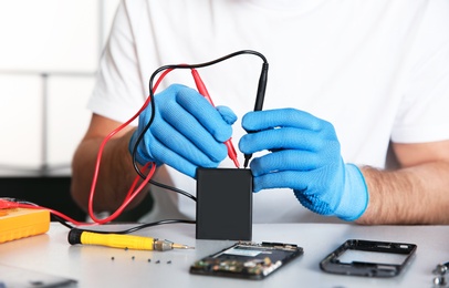 Photo of Technician checking mobile phone battery at table in repair shop, closeup