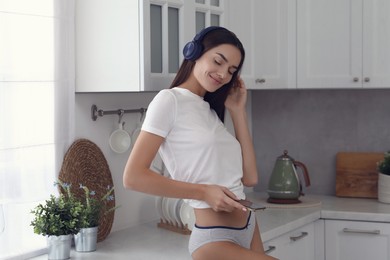 Photo of Young woman in white t-shirt and comfortable underwear listening to music indoors