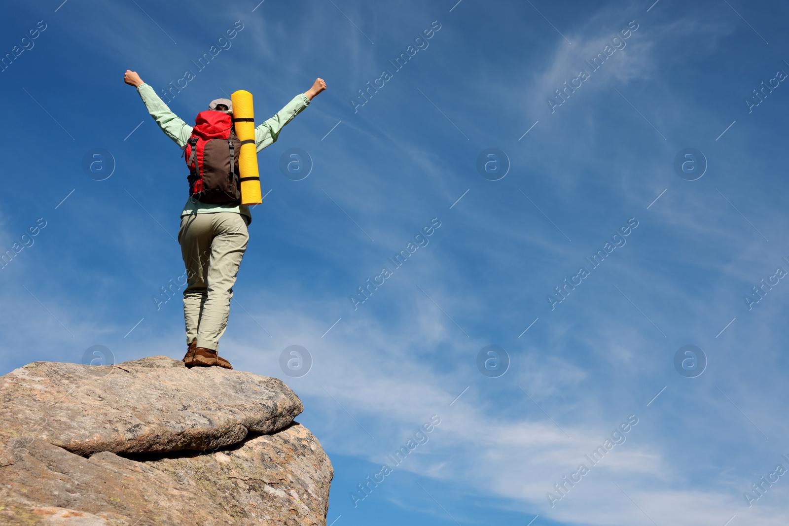 Photo of Young woman with backpack and sleeping mat on cliff, back view. Space for text