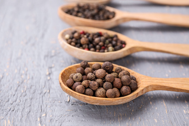 Photo of Spoons with peppercorns on grey wooden table, closeup