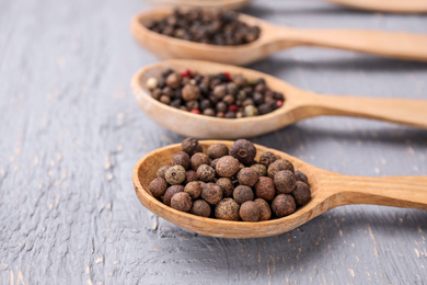 Spoons with peppercorns on grey wooden table, closeup