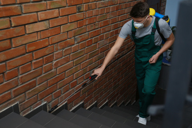 Photo of Pest control worker spraying pesticide on stairs indoors. Space for text