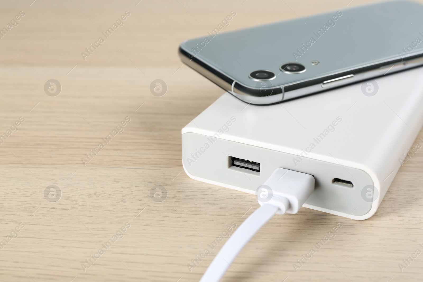 Photo of Mobile phone and portable charger on wooden background, closeup. Space for text