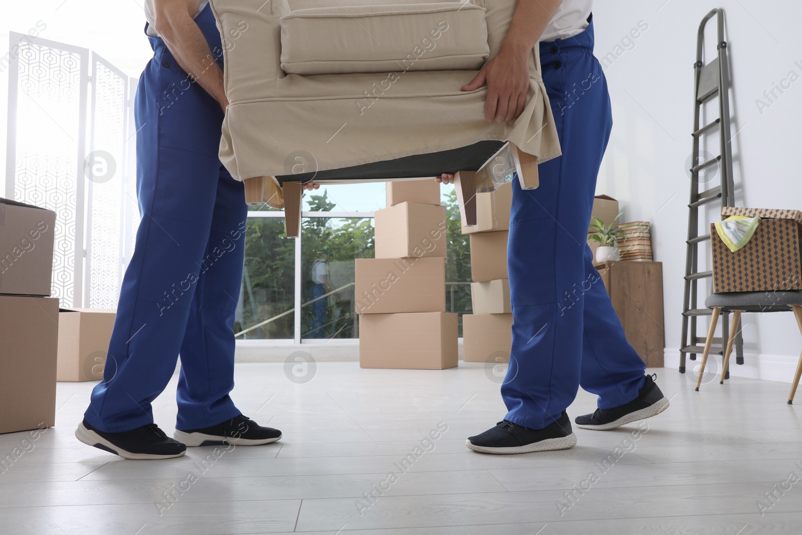 Photo of Moving service employees carrying armchair in room, closeup