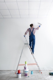 Photo of Male decorator painting wall with roller in empty room
