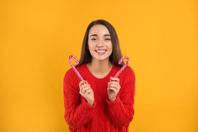 Young woman in red sweater holding candy canes on yellow background. Celebrating Christmas