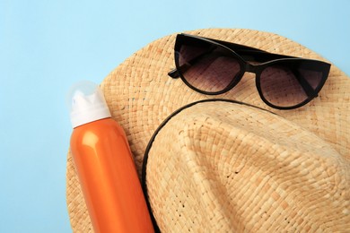 Bottle of sunscreen and beach accessories on light blue background, top view