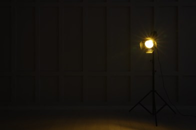 Photo of Bright yellow spotlight near wall in dark room, space for text
