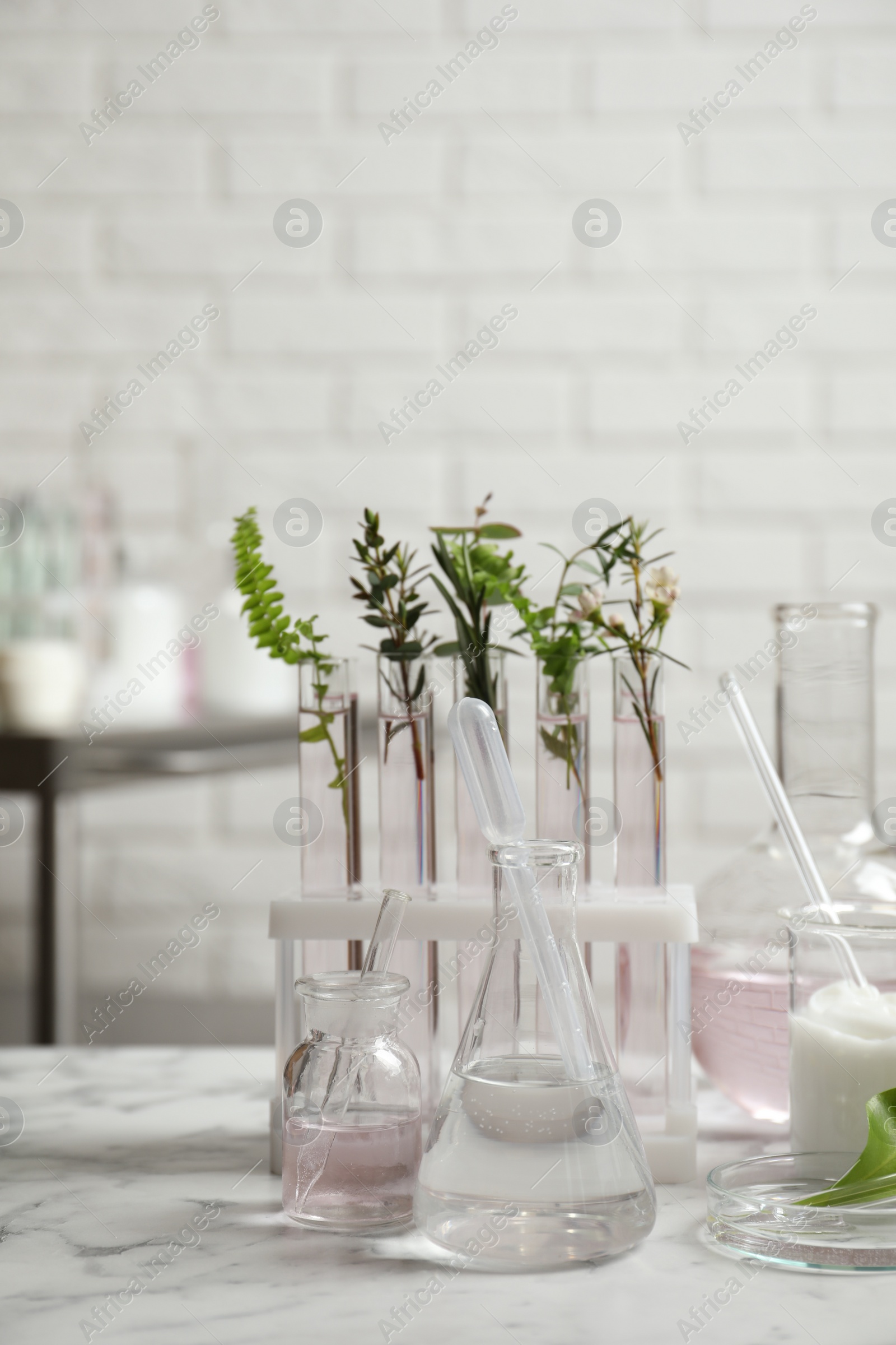 Photo of Natural ingredients and laboratory glassware for organic cosmetic product on white marble table