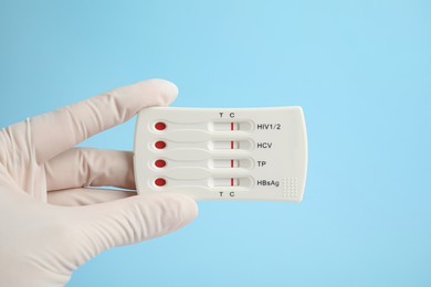 Photo of Doctor holding disposable express test for hepatitis on light blue background, closeup