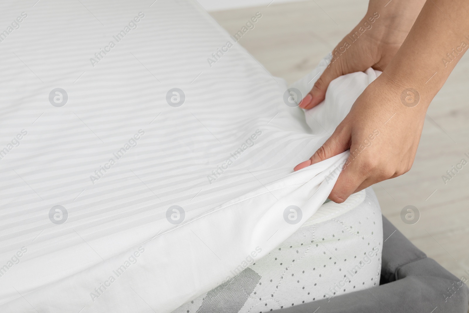 Photo of Woman putting cover on mattress indoors, closeup