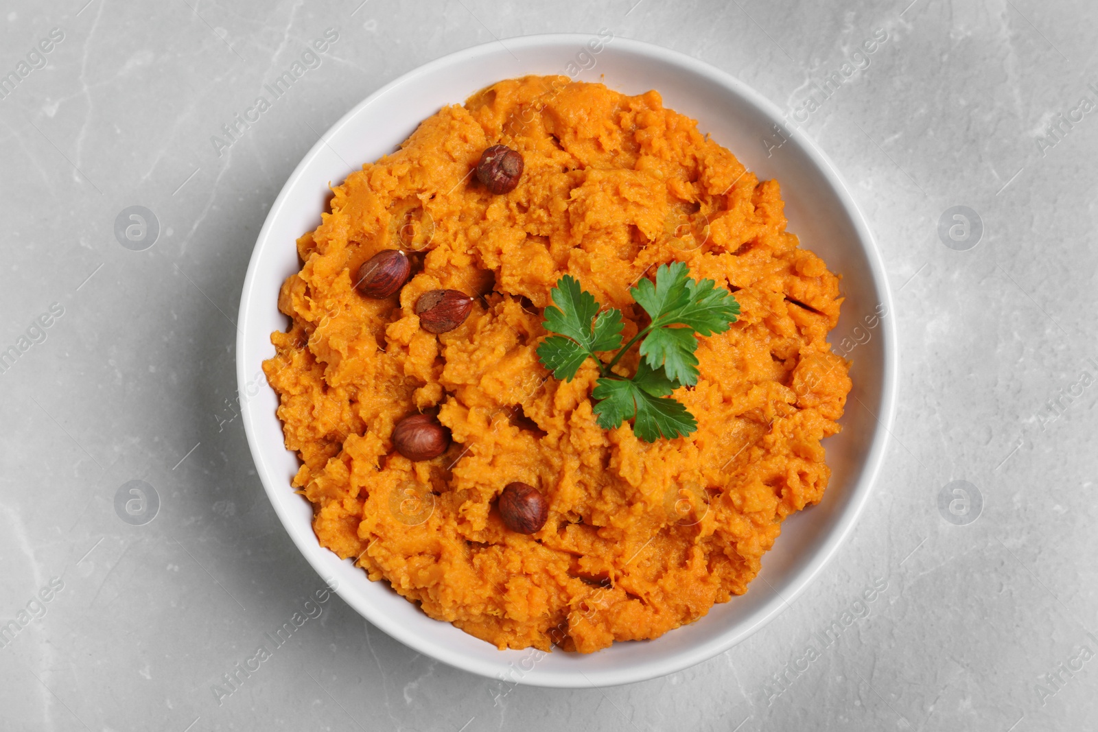 Photo of Bowl of tasty sweet potato puree on grey marble table, top view