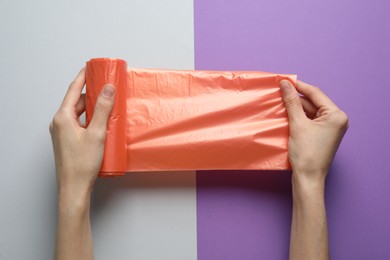 Woman holding roll of orange garbage bags over color background, top view