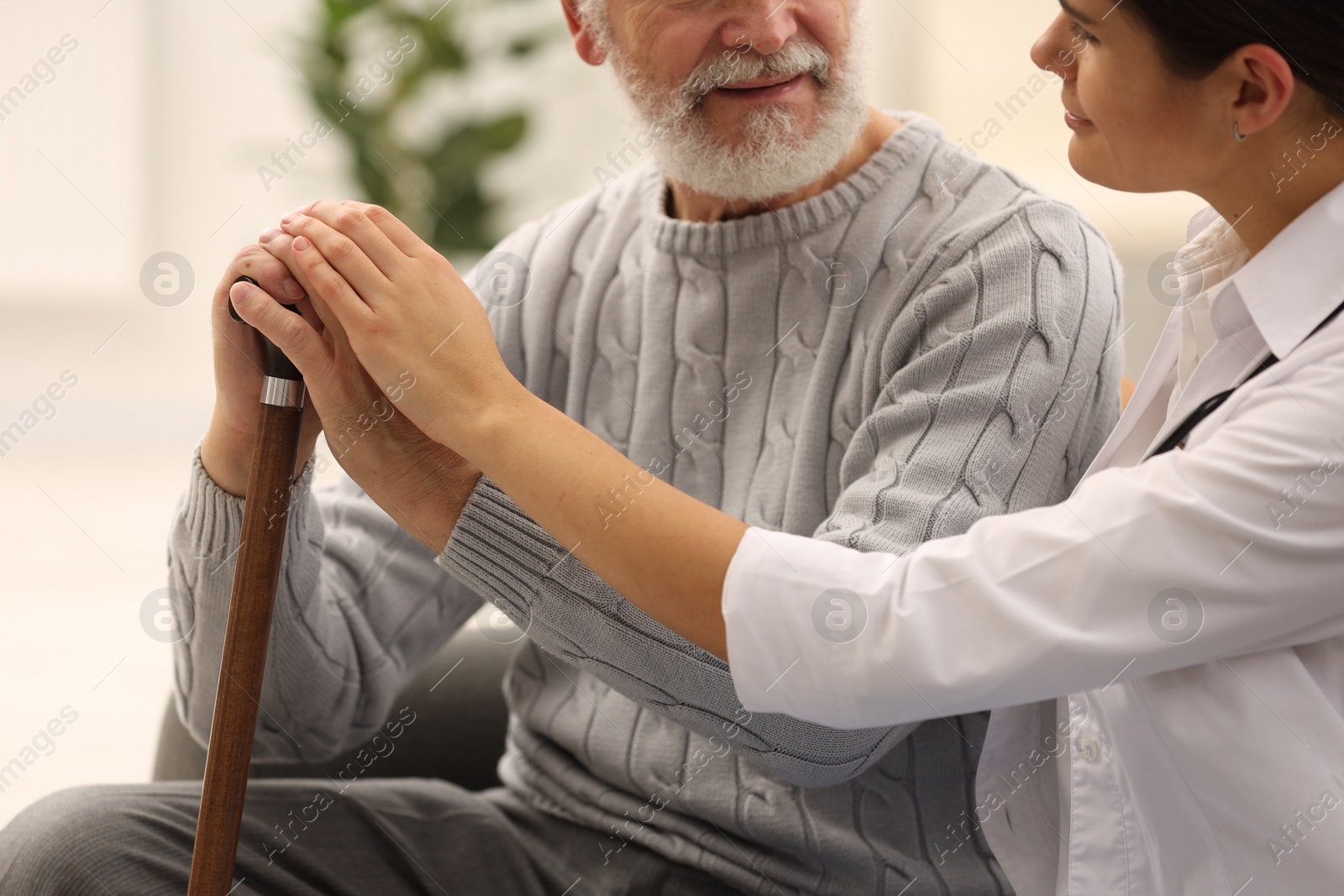 Photo of Nurse supporting elderly patient indoors, closeup view