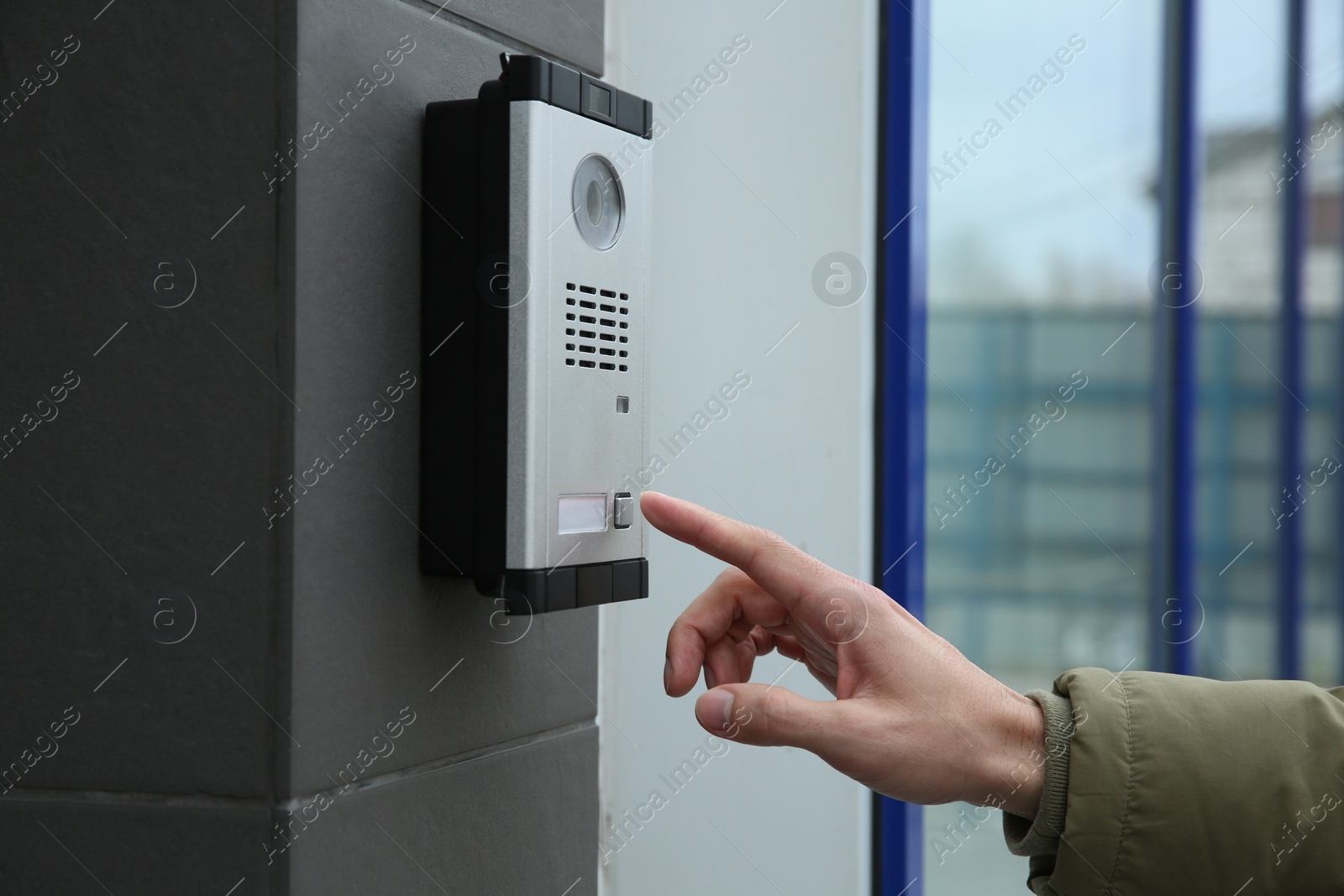 Photo of Man ringing intercom with camera near building entrance, closeup