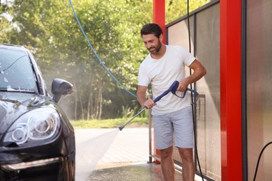Photo of Happy man washing auto with high pressure water jet at outdoor car wash