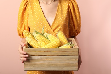 Woman with crate of corn cobs on coral background, closeup