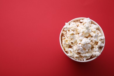 Photo of Paper bucket with delicious popcorn on red background, top view. Space for text