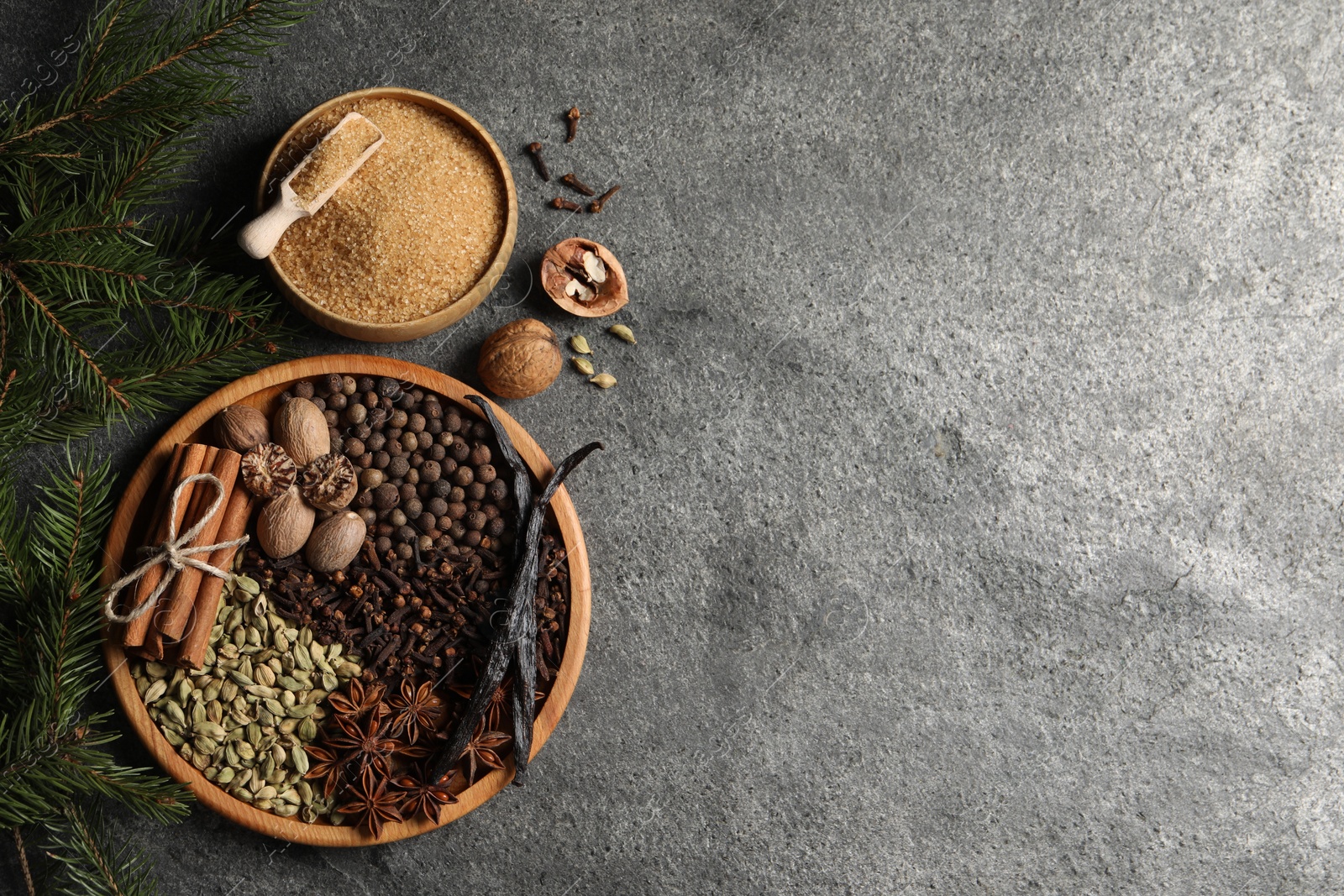 Photo of Different spices, nuts and fir branches on gray textured table, flat lay. Space for text