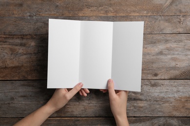 Photo of Woman with blank brochure on wooden background, above view. Mock up for design