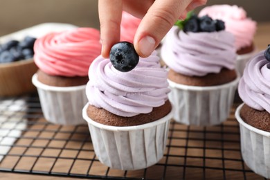 Photo of Woman decorating cupcake with fresh blueberry at table, closeup