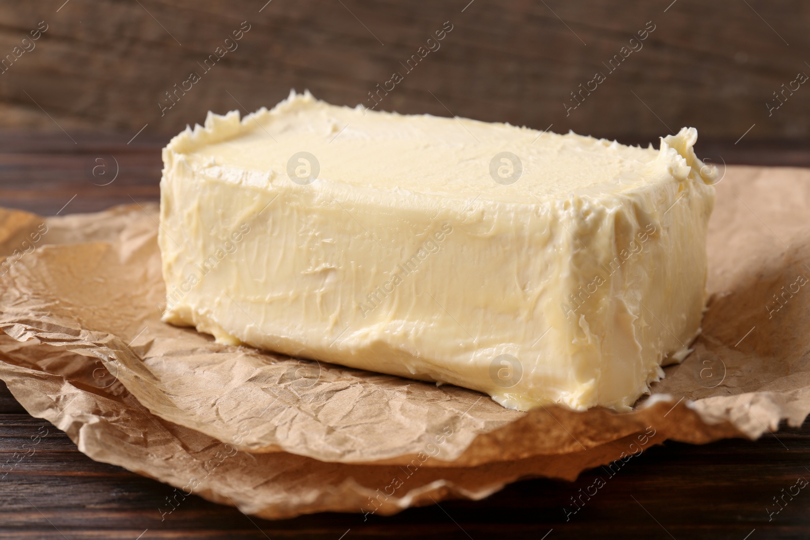 Photo of Parchment with piece of tasty homemade butter on wooden table, closeup