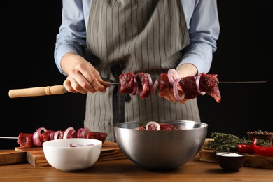 Woman stringing marinated meat on skewer at wooden table, closeup