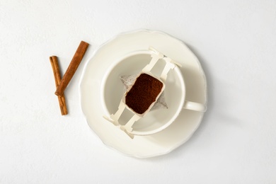 Photo of Drip coffee in cup and cinnamon on white table, flat lay