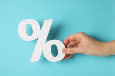 Photo of Woman holding percent sign on light blue background, closeup