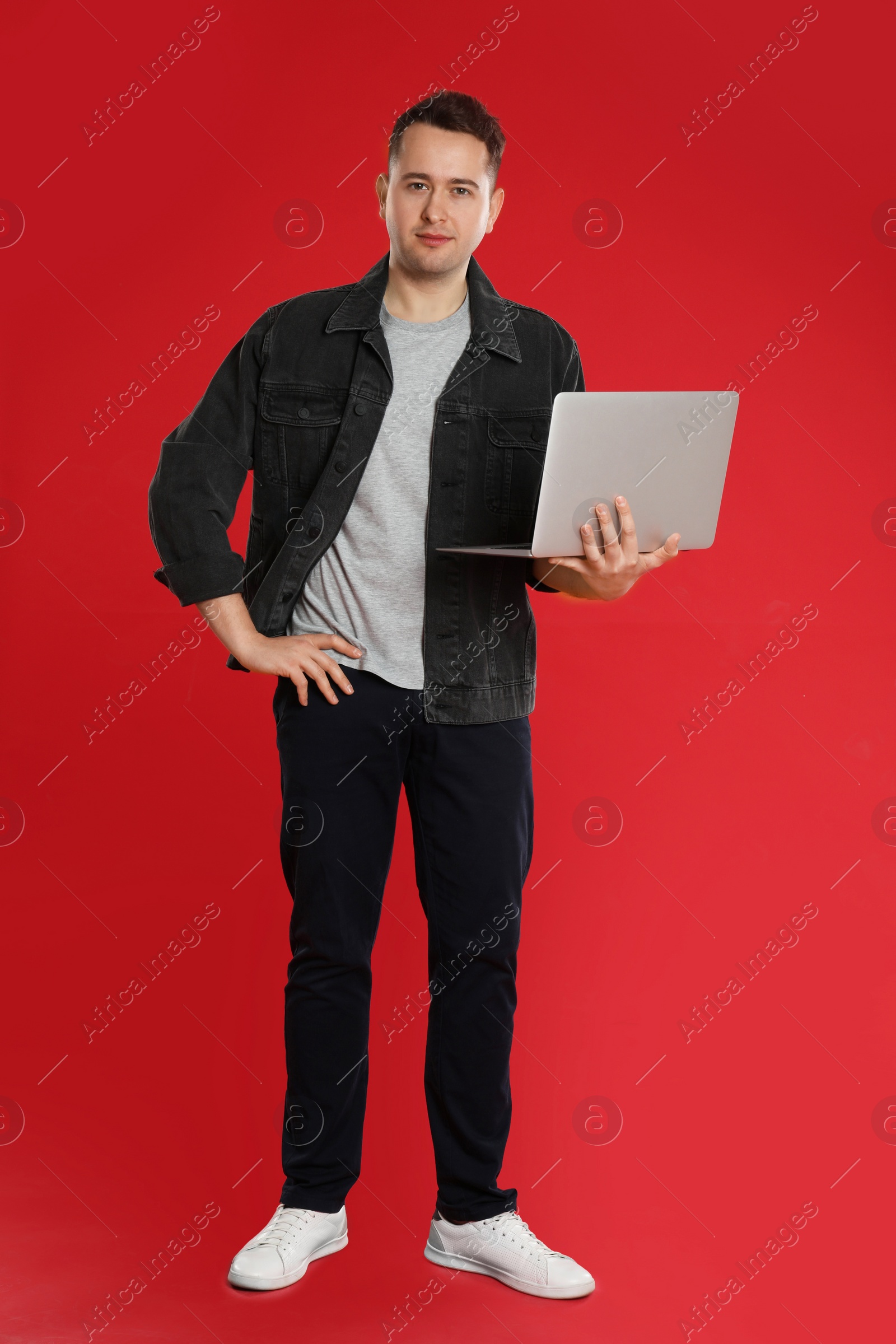 Photo of Young man holding laptop on red background