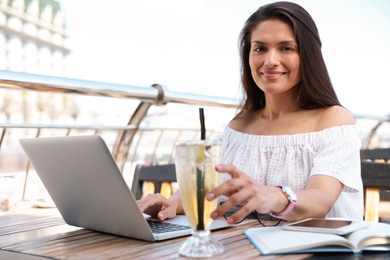 Photo of Beautiful woman with refreshing drink and laptop at outdoor cafe