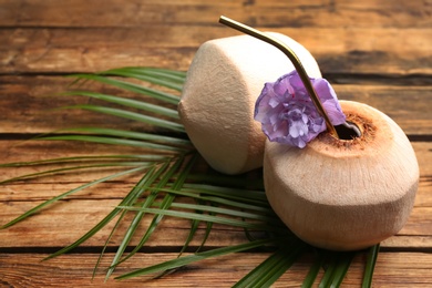 Photo of Fresh coconut with drinking straw and flower on wooden table. Space for text