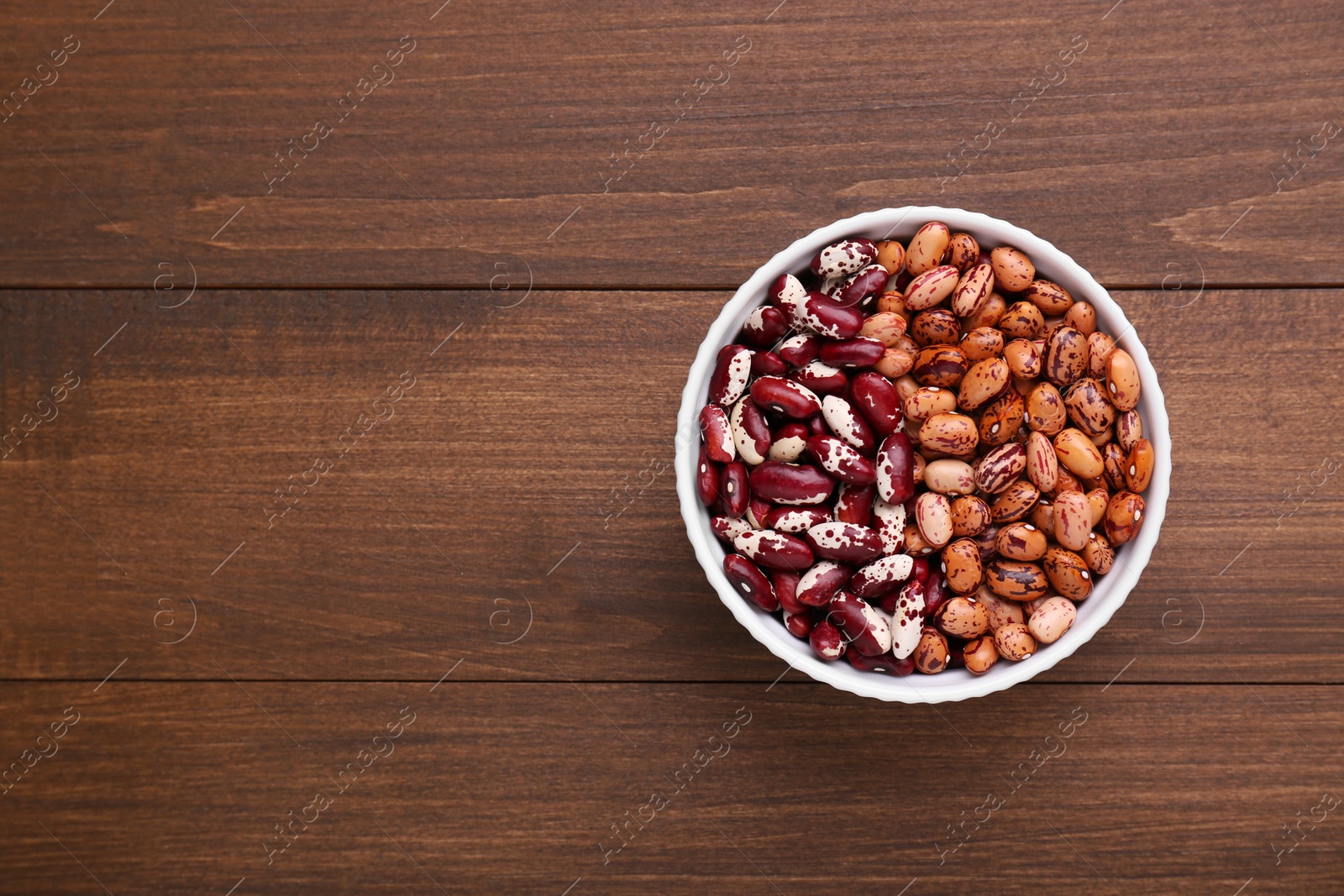 Photo of Different kinds of dry kidney beans in bowl on wooden table, top view. Space for text