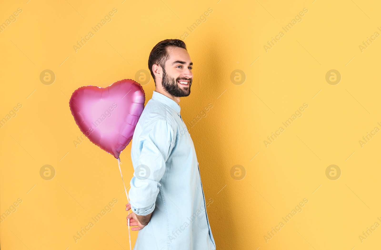 Photo of Portrait of young man with heart shaped balloon on color background. Space for text