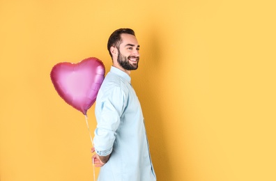 Portrait of young man with heart shaped balloon on color background. Space for text