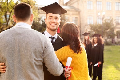 Photo of Happy student with parents after graduation ceremony outdoors