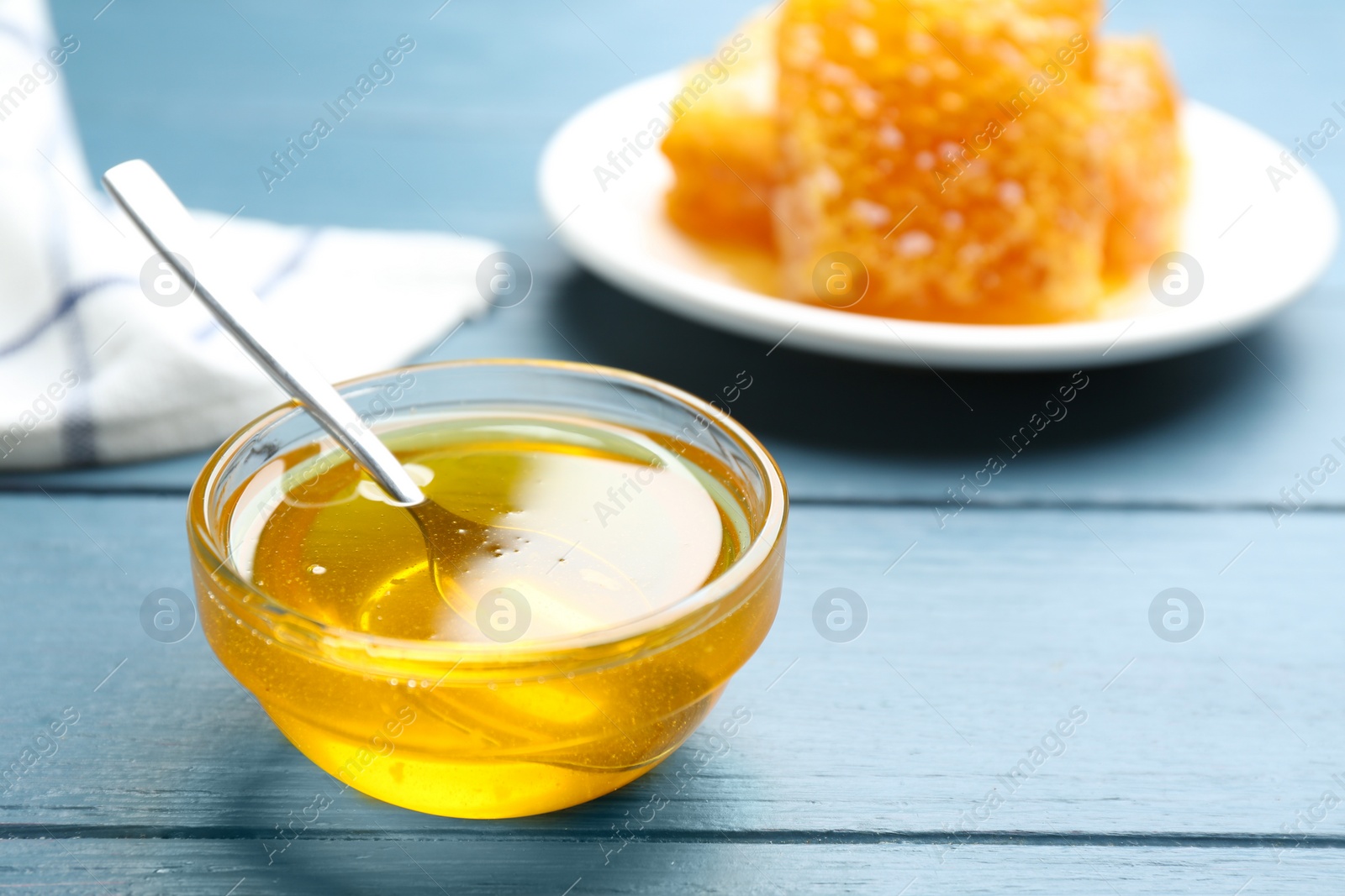 Photo of Fresh honey in bowl on blue wooden table, space for text